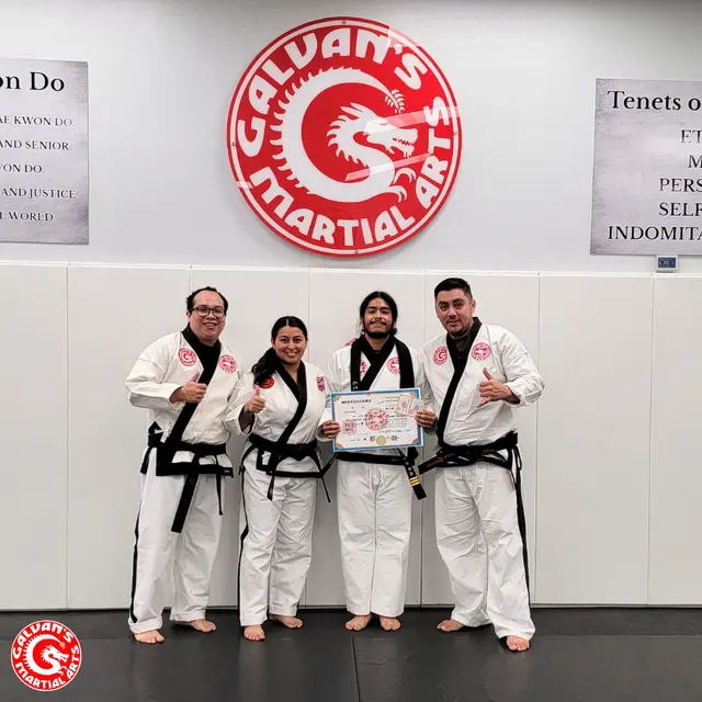 Instructors in black belts with a student holding a certificate at Galvan's Martial Arts